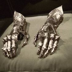 two metal gloves sitting on top of a pillow covered in silver paint and rivets