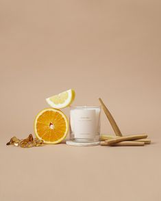 an orange, lemon and cinnamon stick next to a candle on a brown background with some other items