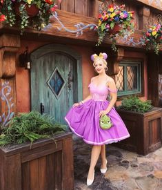 a woman standing in front of a house wearing a purple dress and holding a green purse