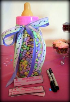 a baby bottle filled with candy next to some writing utensils on a table