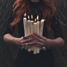 a woman with red hair holding candles in her hands