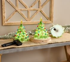 two green christmas trees on a table with a remote control in the foreground and a wooden frame behind them