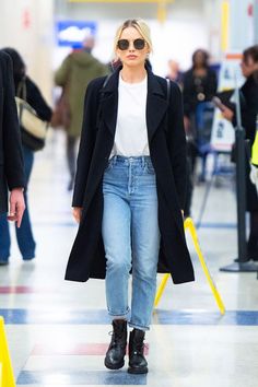 a woman in black coat and jeans walking through an airport