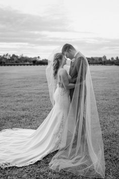 a bride and groom kissing on the grass in front of an open field with trees