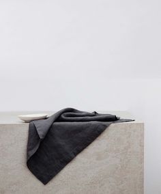 a folded black cloth sitting on top of a white table next to a vase with flowers