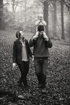 a man and woman walking in the woods with a baby on their shoulders while holding hands