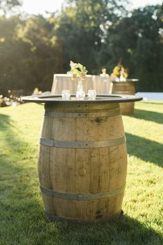 a wooden barrel table with flowers on it in the middle of a grassy area at a wedding