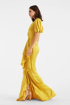 a woman in a yellow dress is standing up and looking off to the side with her hand on her hip