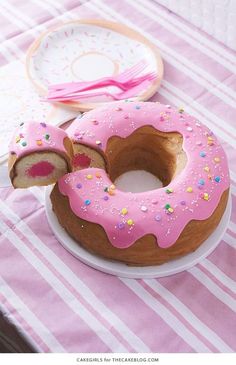 a pink frosted donut on a plate with a slice taken out of it