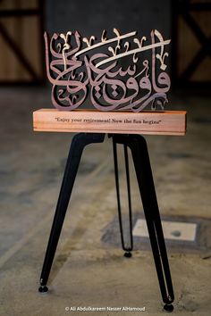 an intricately designed wooden chair with arabic writing on the back and sides, sitting on top of a black metal tripod