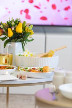 a table topped with plates and bowls filled with food next to a vase full of flowers