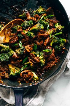 a skillet filled with beef and broccoli on top of a white table