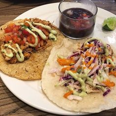 two tacos on a white plate next to a bowl of salsa and a drink