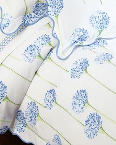 a bed with blue flowers on it and white sheets that have green trim around the edges