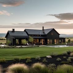 a large black house sitting on top of a lush green field with mountains in the background