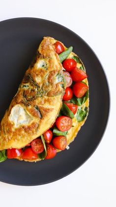 an omelet with tomatoes and spinach on a black plate, ready to be eaten