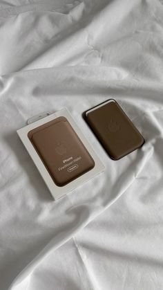 two brown and white electronic devices laying on top of a white bed sheet covered in sheets