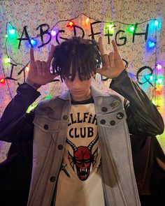 a young man with dreadlocks standing in front of a wall covered in lights