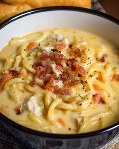 a bowl filled with pasta and bacon on top of a table next to some bread