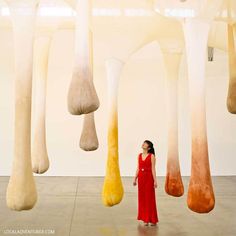 a woman in a red dress standing next to some tall white and orange objects hanging from the ceiling