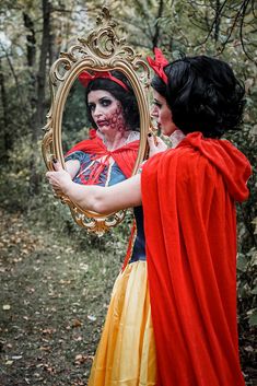 two women dressed as snow white and the evil queen looking at herself in a mirror