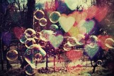 soap bubbles are floating in the air near trees and hearts shaped shapes on a sunny day