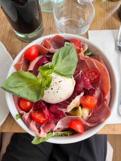 a white bowl filled with meat and veggies on top of a wooden table