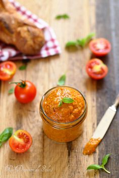 a jar filled with tomato sauce sitting on top of a wooden table next to sliced tomatoes