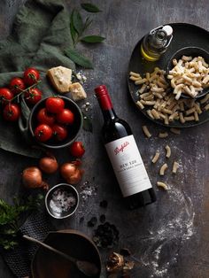 a bottle of wine sitting next to some food on top of a wooden table with tomatoes and other ingredients