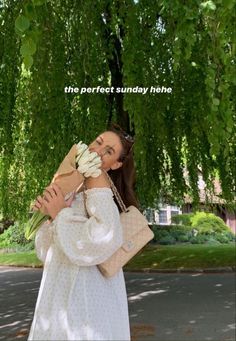 a woman standing under a tree holding a bunch of flowers in her hands and looking at the camera