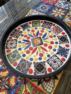 a decorative tray on top of a table covered in colorful tiles and designs with black rim