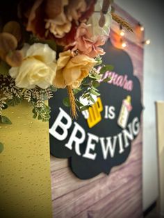 there is a sign that says beer is brewing and flowers are in front of it