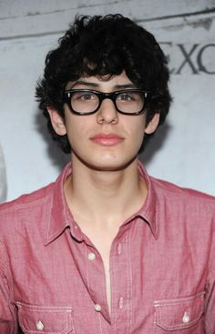 a young man wearing glasses standing in front of a wall