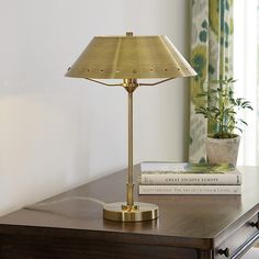 a lamp sitting on top of a wooden table next to a book and potted plant