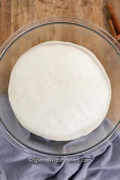 dough in a glass bowl with cinnamon sticks next to it on a wooden table top