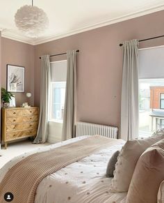 a bedroom with pink walls and white bedding, beige curtains on the windowsill