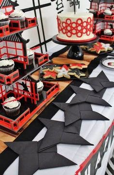 a table topped with cakes and cupcakes covered in black paper cranes on top of it