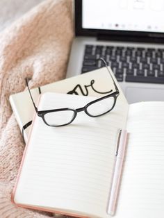 an open notebook with glasses on it next to a laptop