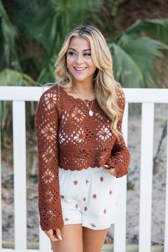 a woman standing in front of a white fence wearing a brown crochet sweater