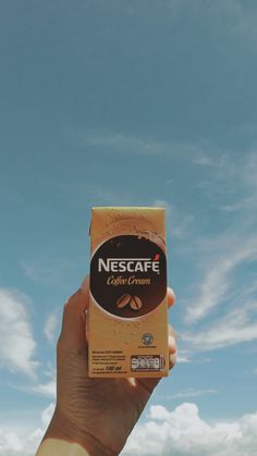 someone holding up a box of coffee in their hand with the sky in the background