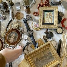 a table topped with lots of different types of framed pictures and other antique items next to a person's hand