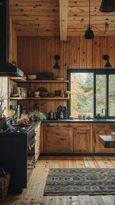 a kitchen with wooden walls and flooring next to an open window that looks out onto the woods