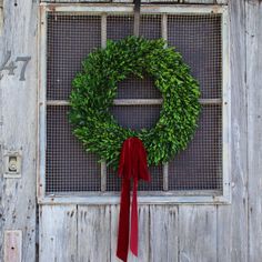 a wreath is hanging on the side of a wooden door with a red ribbon tied around it