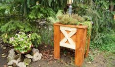 a wooden planter with plants in it next to a tree and rocks on the ground