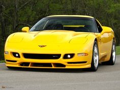 a yellow sports car driving down a road next to some trees and bushes in the background