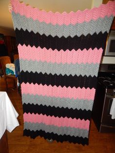 a pink, black and gray knitted blanket sitting on top of a wooden floor