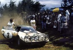 an old race car being driven by two men in front of people on the grass