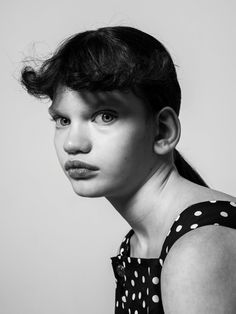 a black and white photo of a woman with polka dots on her dress looking at the camera