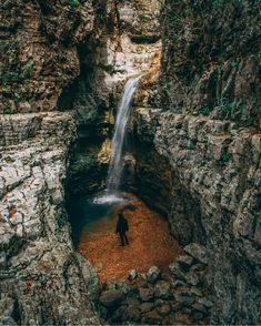 a man standing in the middle of a canyon with a waterfall coming out of it