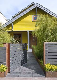 a yellow house with wooden fence and plants on the front yard in front of it